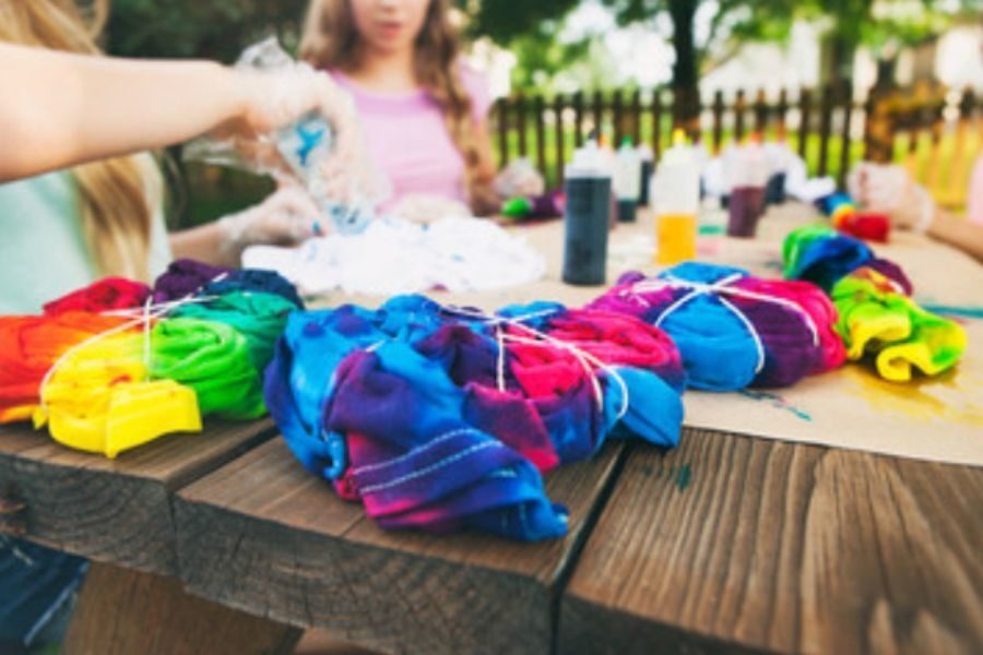 Children tie dying t-shirts on rustic wooden table