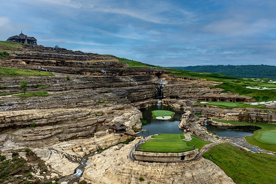 a putting green at the bottom of a mountainous rock formation is surrounded by water on all sides. paynes valley hole 19