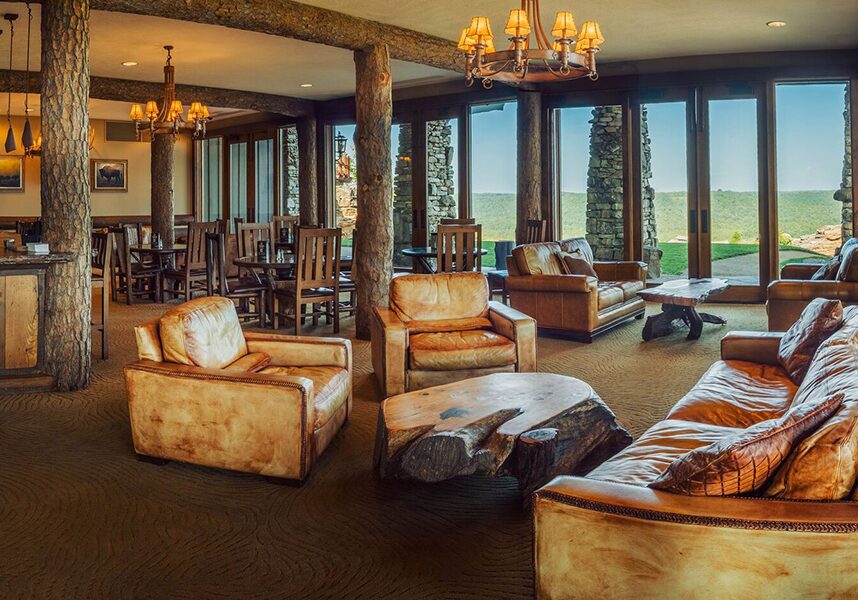 mountain top lounge with tan chairs and floor to ceiling windows overlooking the golf course