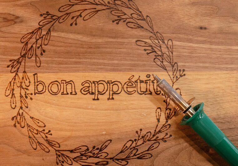 A Woden cutting board with a wood burned design rigged around the words "Bon Appetite"