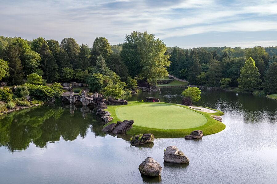 a putting green is surrounded by a pond where large boulders poke out of the water