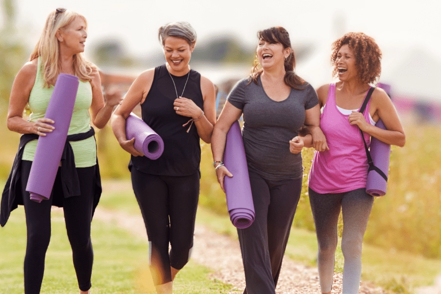 group of women in athletic attire walking and laughing with yoga mat rolled under their arms