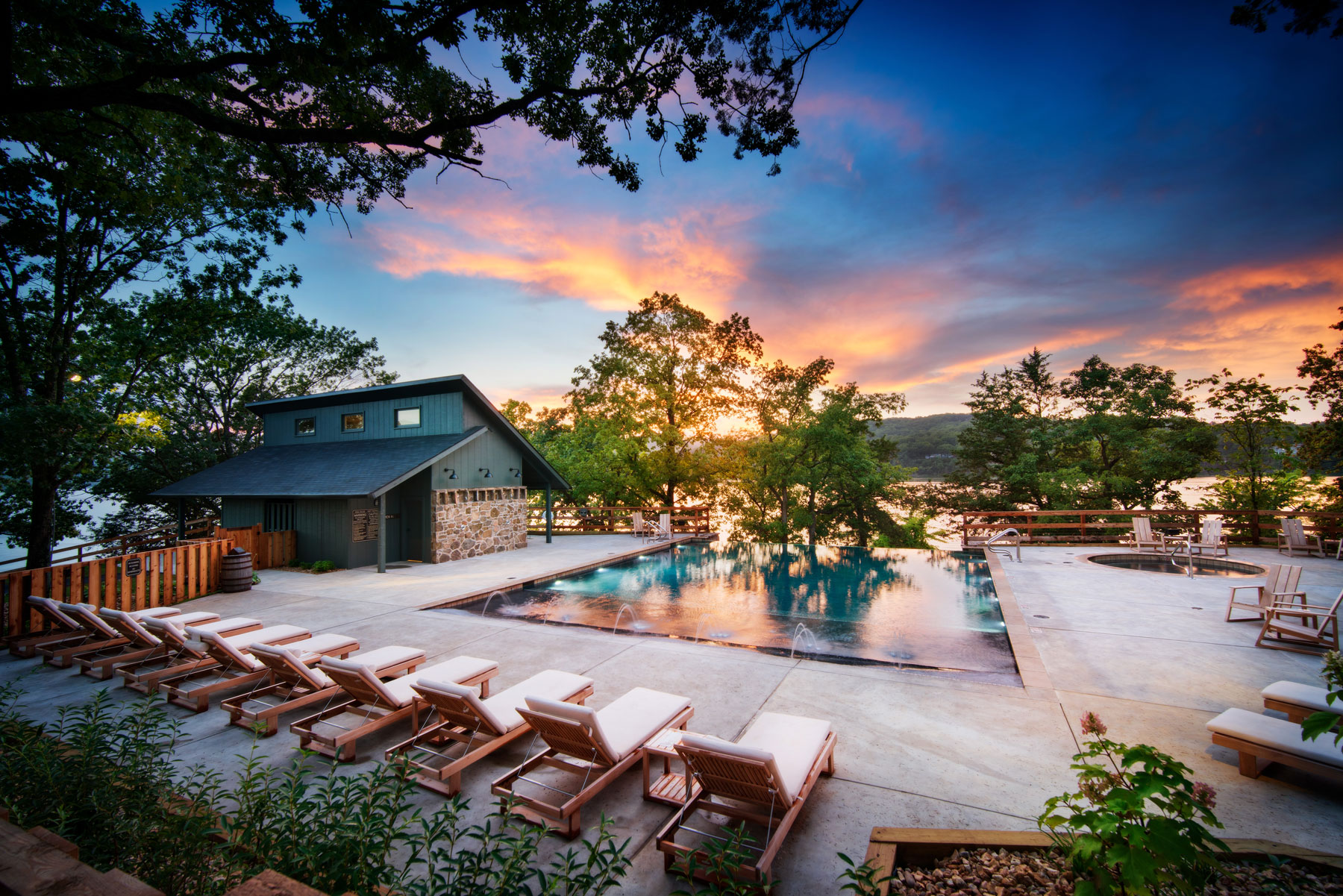 Camp Long Creek swimming pool lined with reclining chairs, vivid sunset and lake in the background
