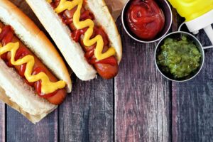Two hotdogs with relish and ketchup on a rustic wooden table