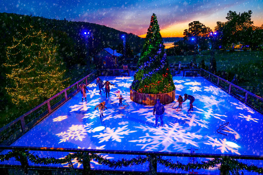 Big Cedar's Ice-Rink at night with projected snowflakes on the ice and large Christmas tree in the center.