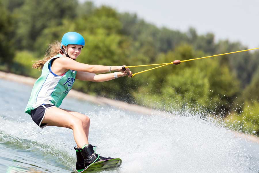 Woman wakeboarding on the lake with thick foliage in the background