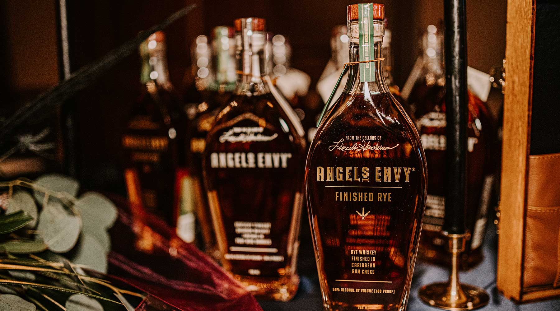 Multiple bottles of Angel's Envy sit on a rustic bar with a mirror back.