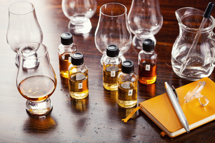 Bourbon bottles and pipettes strewn across a wooden table with notetaking supplies