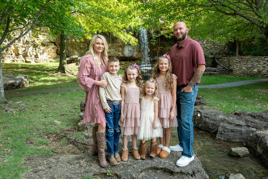 A family poses in front of a waterfall in casual westerner for a family portrait