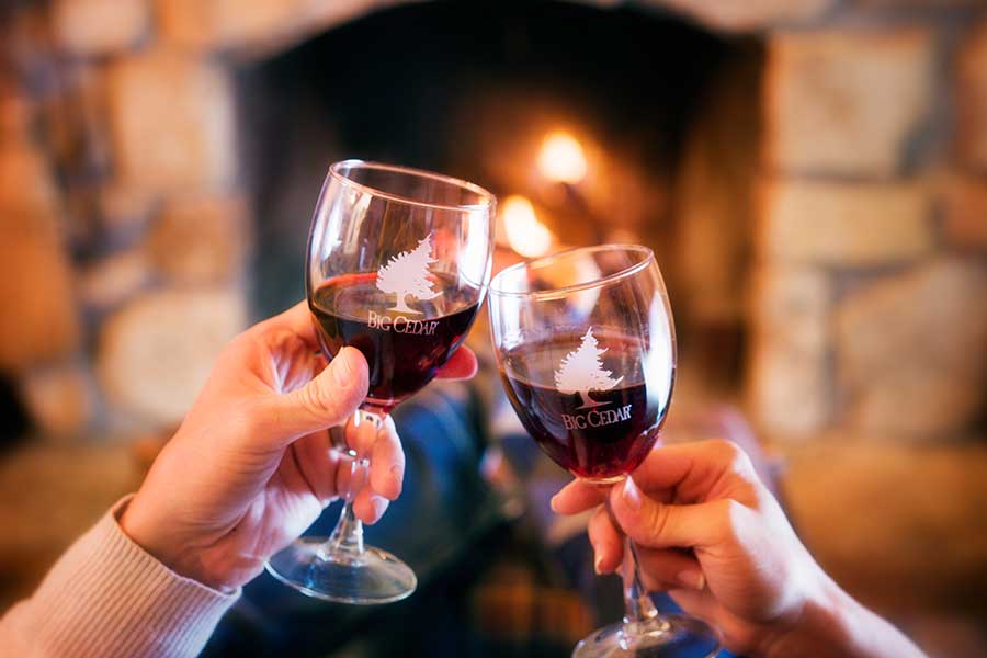 Couple toasting with wine glasses in front of a fireplace at Big Cedar Lodge