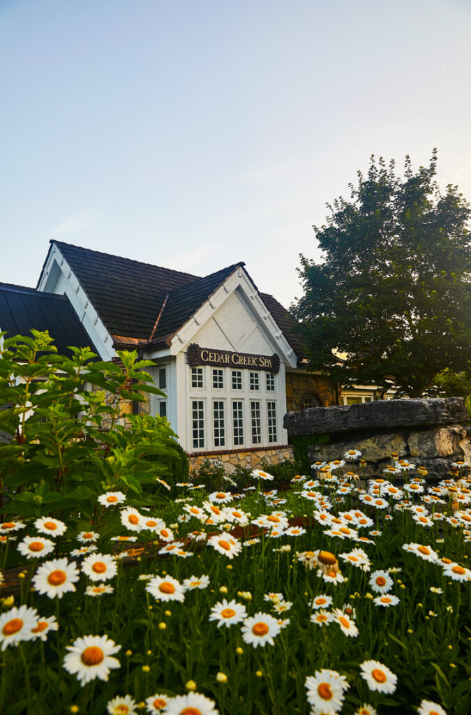 Exterior of Cedar Creek Spa behind a row of blooming daisies.