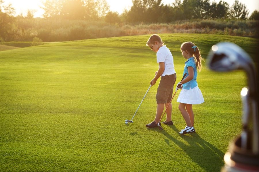 Two children holding golf clubs and preparing to golf.