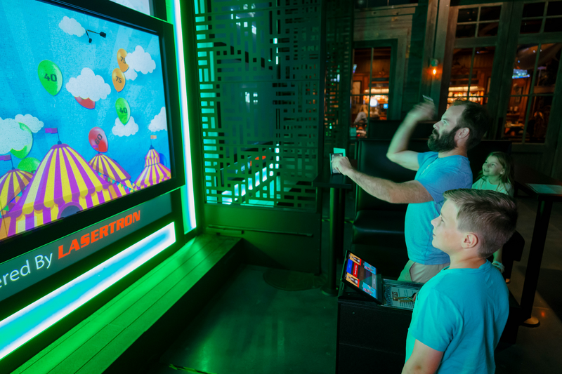 Father and Son throw darts and a projected image of a carnival with balloons of various point values