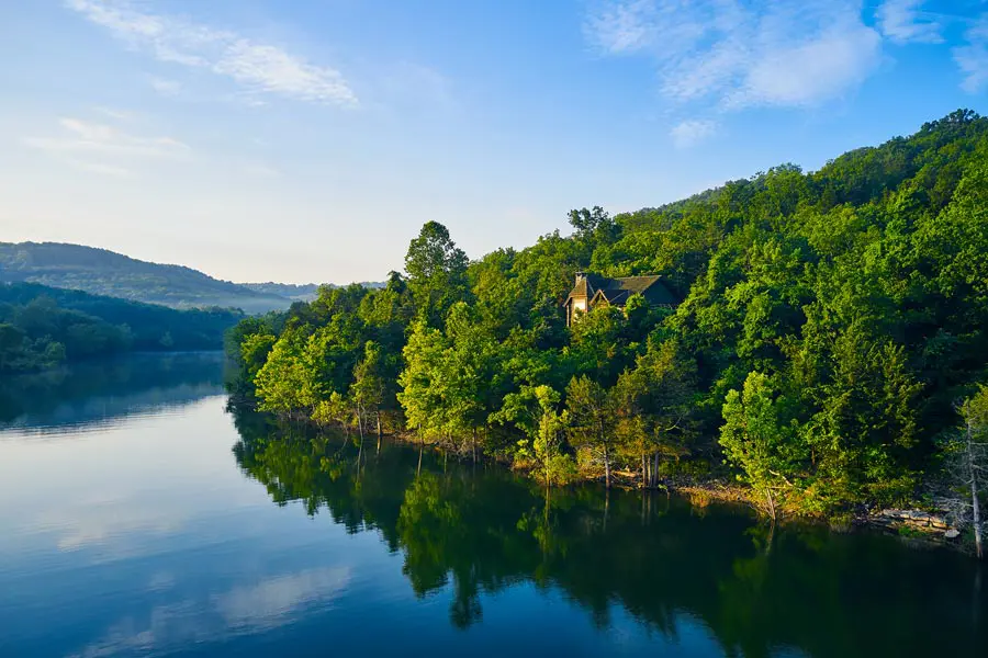 Aerial view of a secluded log cabin nestled in dense green trees along the edge of a calm lake.