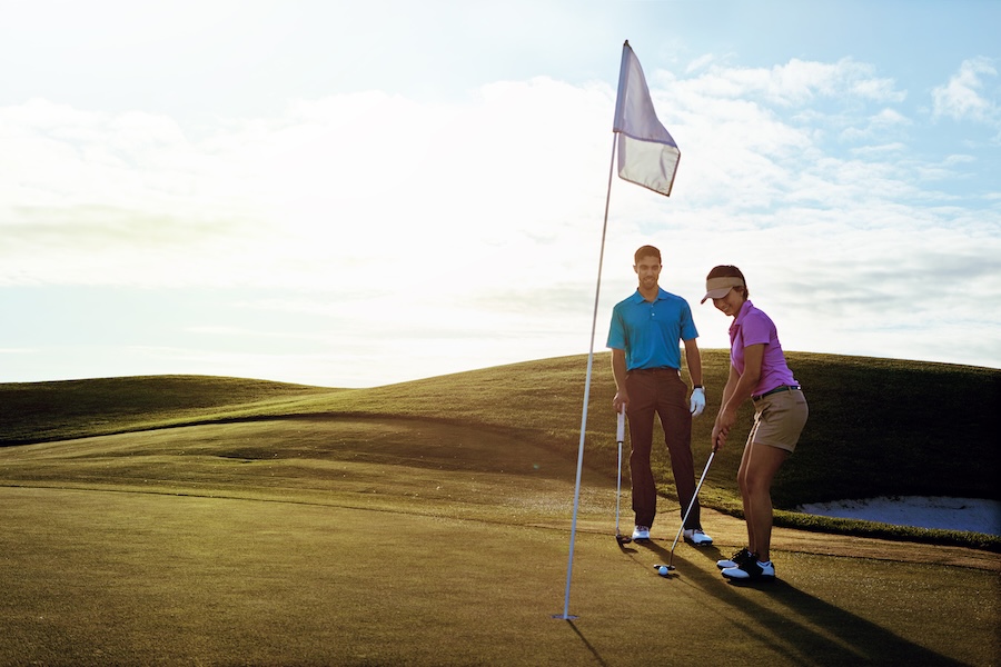 Couple golfing at sunset on a rolling green preparing to putt