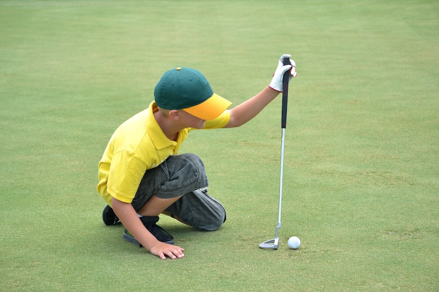 young golfer kneeling to examine the green for his next shot