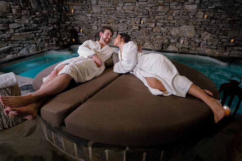 young couple lounges on a circular couch by the stone grotto pool in the Cedar creek spa