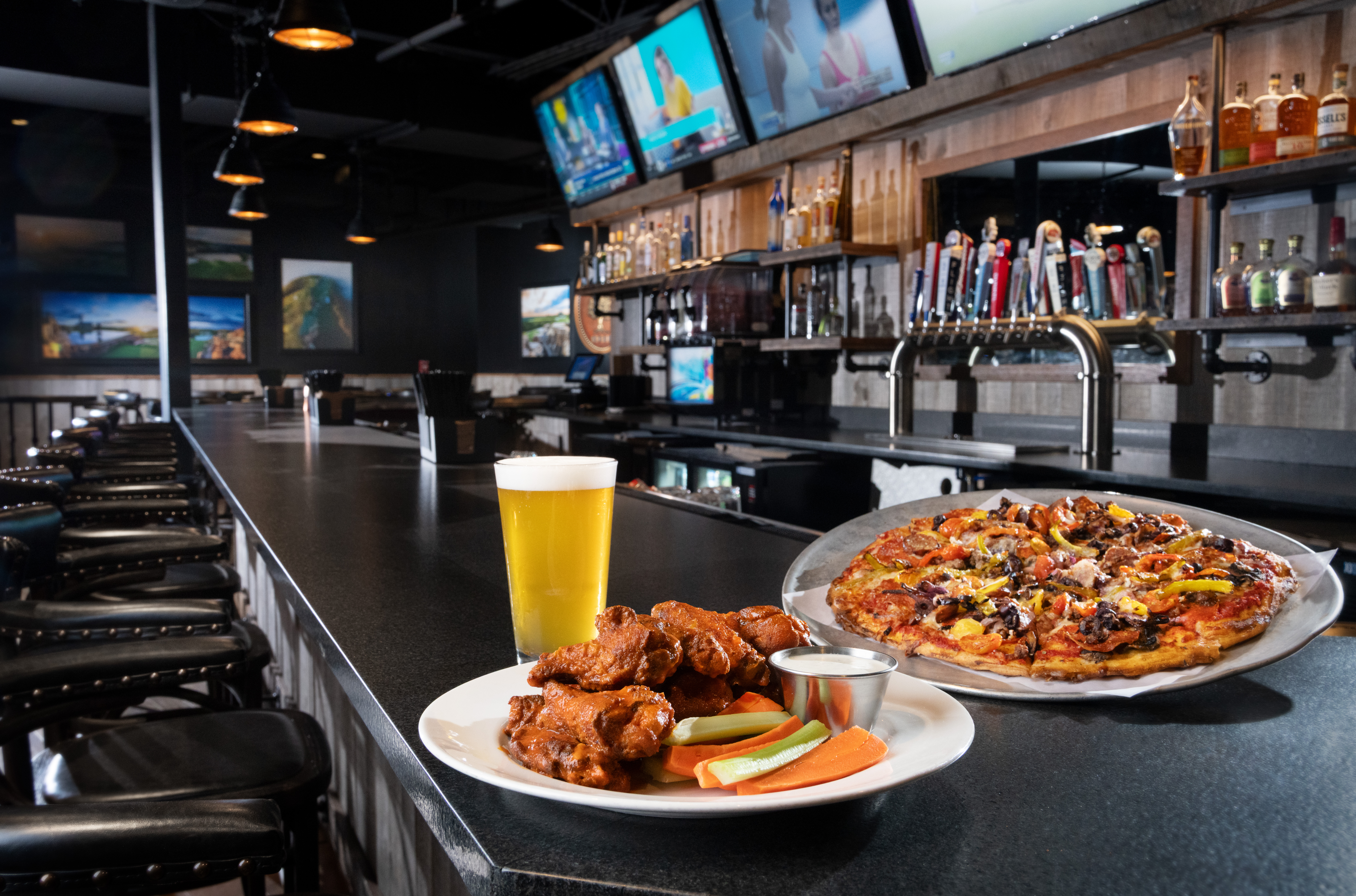 A pizza, a plate of wings, and a glass of beer on the counter at the Bunker Bar