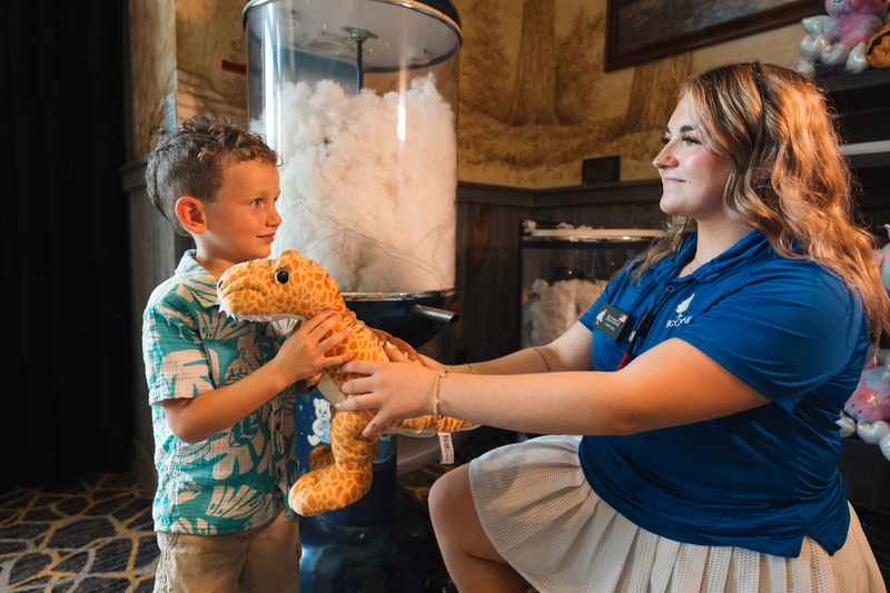 Activity center Attendant passes a freshly stuffed T-Rex Toy to a young boy next to the stuffing machine.
