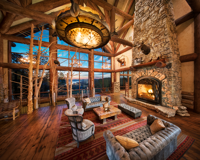 Lobby of the Grandview Conference center with large wooden supports, a stone fireplace that stretches to up into a 2 story vaulted ceiling, rustic leather furniture, whole sun bleached cedar trees coming out of the floor, and multi story windows overlooking Table Rock lake and the Ozarks mountains