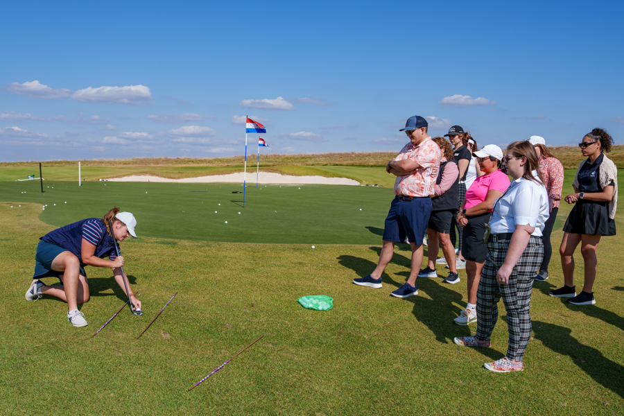 a group watches a teachers instruction on a golf course