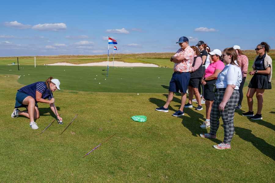 a group watches a teachers instruction on a golf course