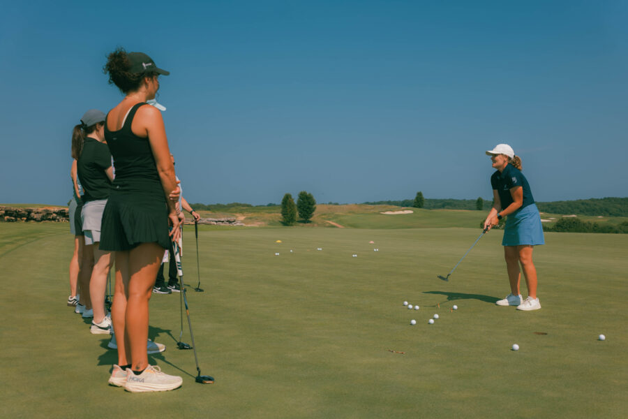 A group on a golf green listen to a golf tutor