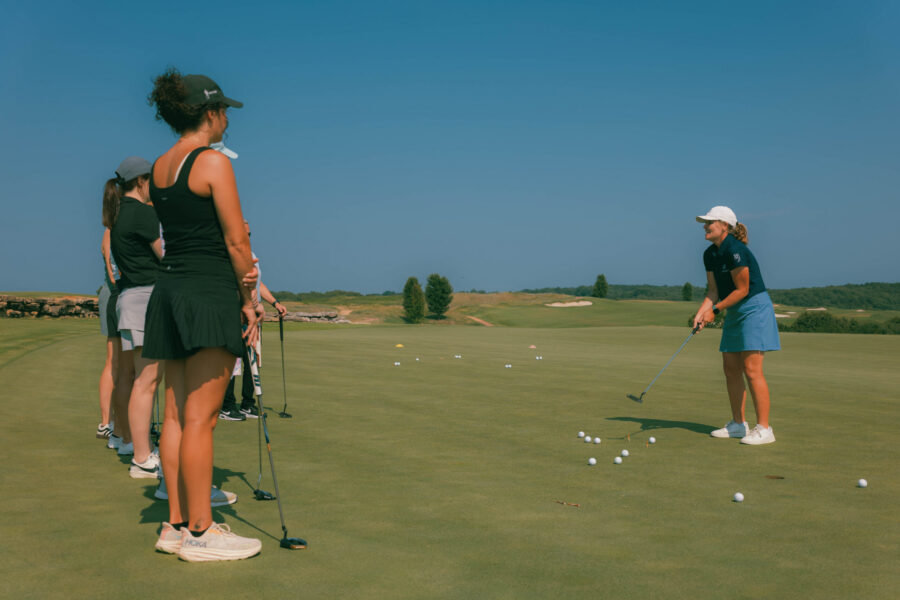 A group on a golf green listen to a golf tutor