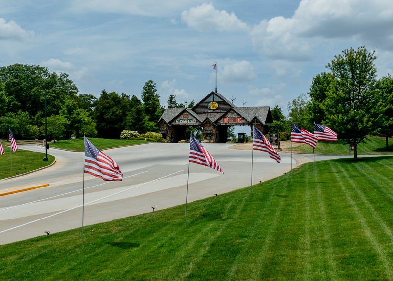 A road lined with American flags leads to a cabin like outdoor structure marking the entrance to Big Cedar Lodge and Top of the Rock