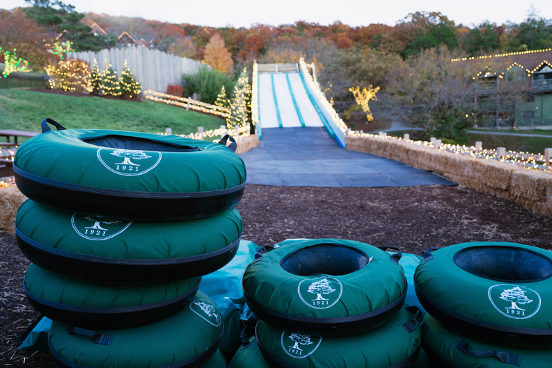 Stacks of dark green inflatable innertubes in front of 4 rows of long white slides enclosed by bales of hay and rounded by autumn trees in the distance