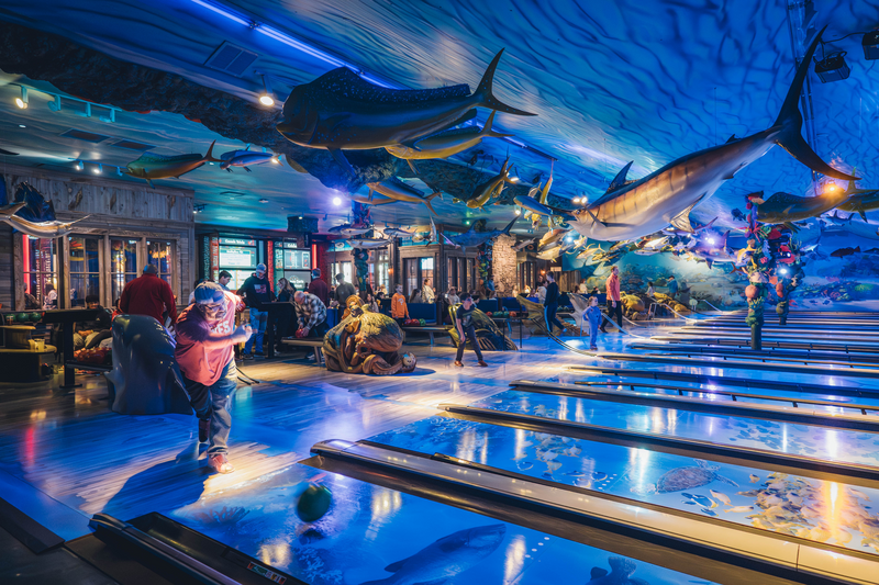 A bowling alley that looks like it is under water with trophy fish hanging from the ceiling and coral fixtures.