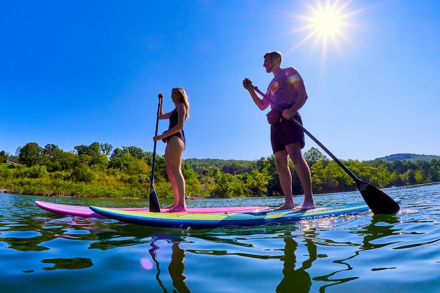 A couple ride on Paddle boards with the sun beaming on the lake