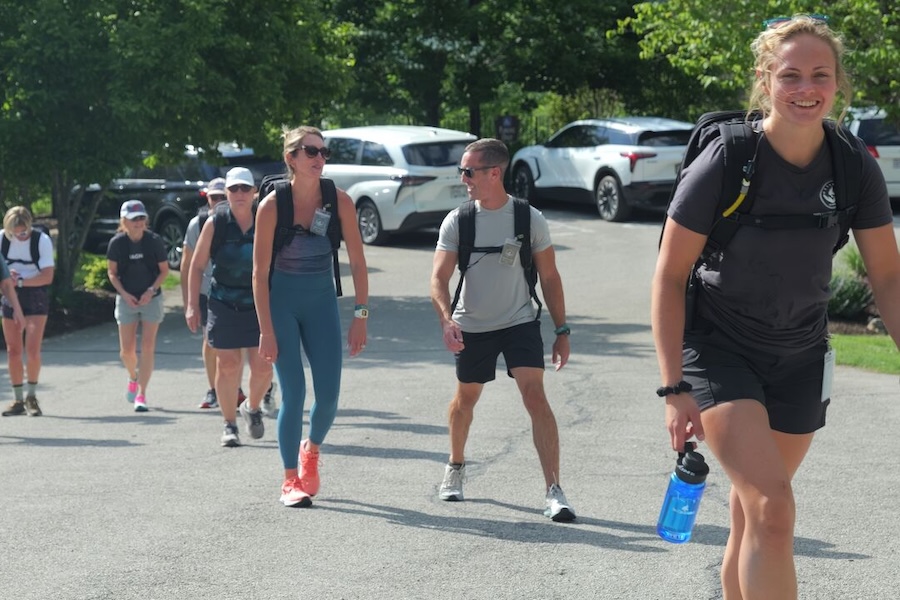 Group walks up a hill carrying weighted back packs