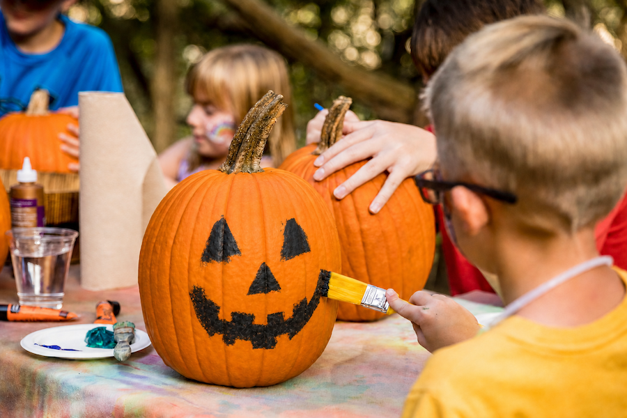 Boy paints jack-o-lantern face onto a pumpkin