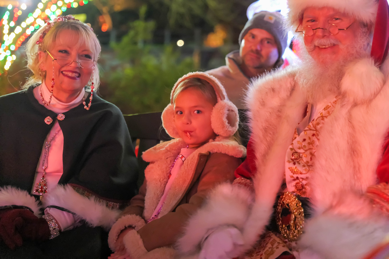 Little girl sits on a red sleigh between Mr. and Mrs. Claus
