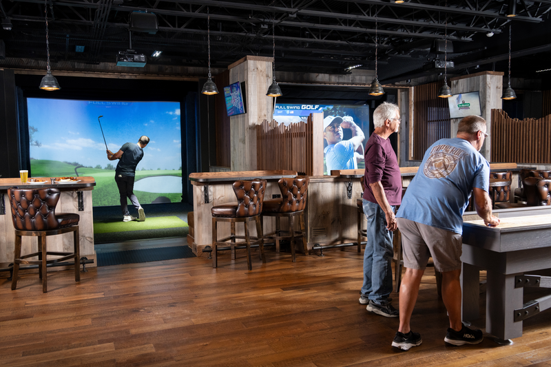 Man plays virtual golf in a simulator bay