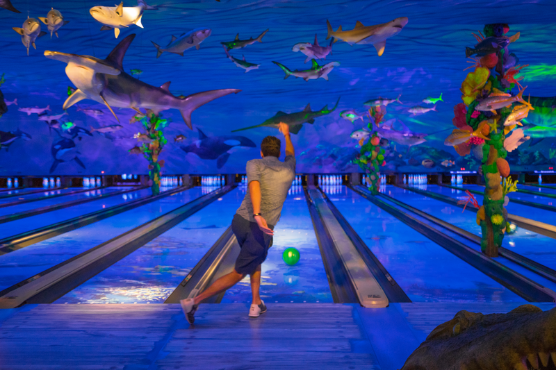 Man throws bowling ball down lane and strike s a diagonal follow through pose