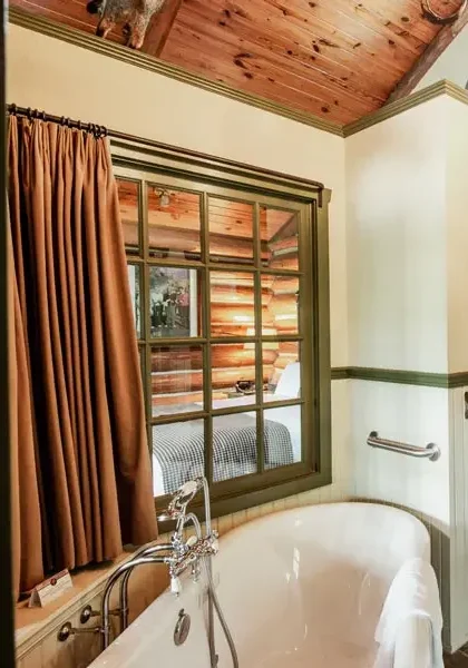 A rustic cabin bathroom featuring a freestanding soaking tub, double vanity, and exposed log walls.