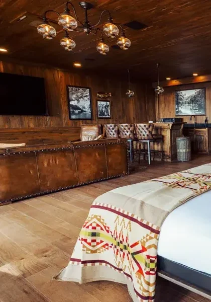 A modern, luxury suite with dark wood-paneled walls and ceiling, a king-size bed, a leather sofa, and a bar area.