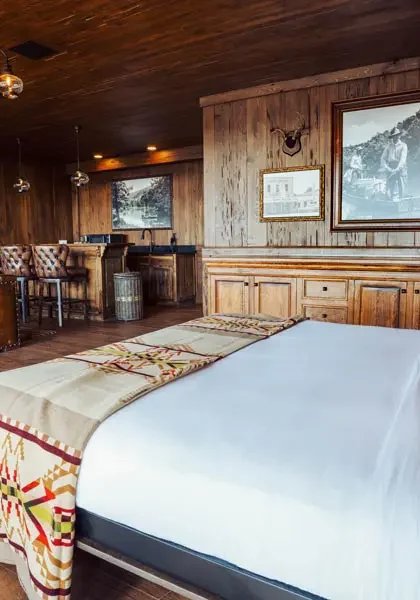 A modern, luxury suite with dark wood-paneled walls and ceiling, a king-size bed, a leather sofa, and a bar area.