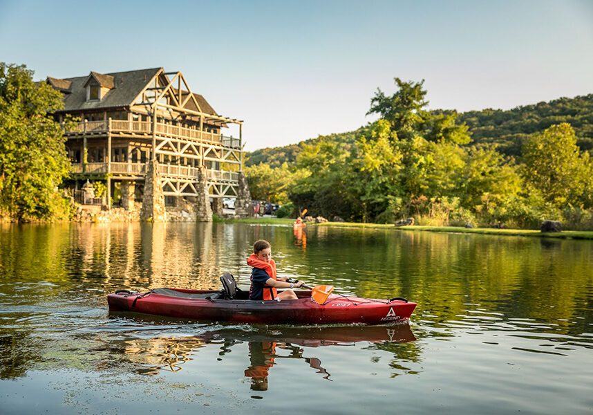 boy in kayak on lake with a large lodge in the background