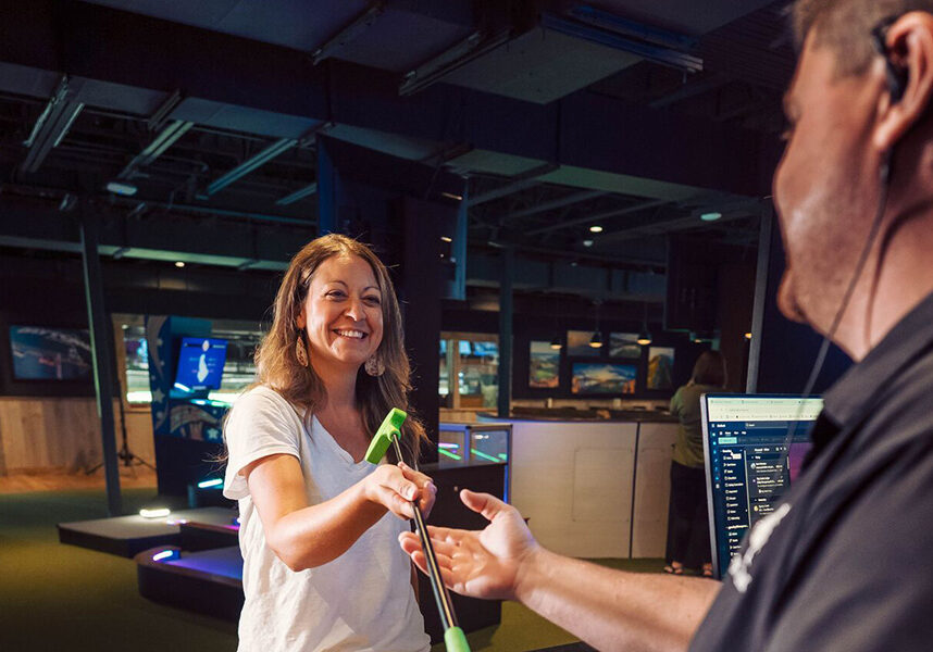 man working at fun mountain hands off a putter to woman about to play lucky putt