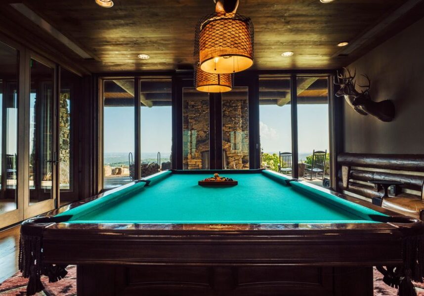 a pool table with in a semi dark room lit by the glow of a hanging lamp