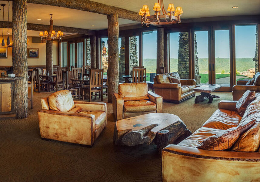 mountain top lounge with tan chairs and floor to ceiling windows overlooking the golf course