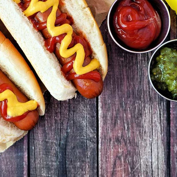 Two hotdogs with relish and ketchup on a rustic wooden table