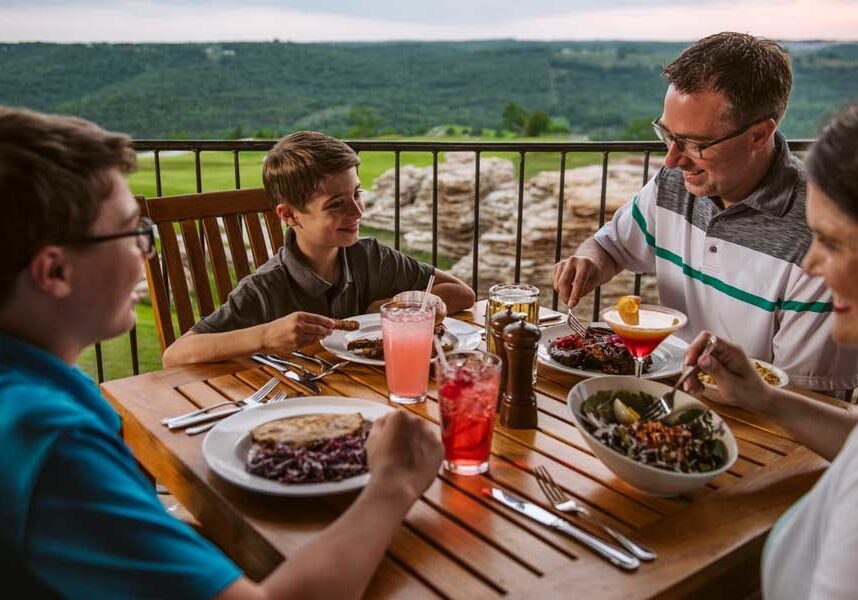 Family of four enjoying a delicious meal overlooking the golf course at Mountain Top Grill