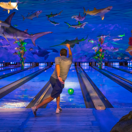 Man throws bowling ball down lane and strike s a diagonal follow through pose