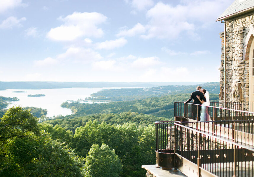 Bride and groom kissing on the balcony of a Big Cedar Top of the Rock chapel with Table Rock Lake in the distance.