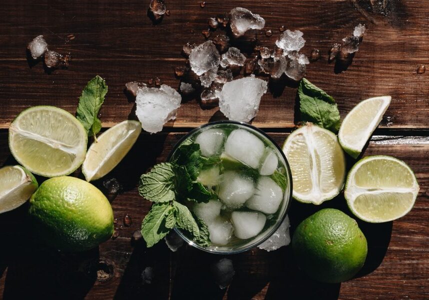 A classic cocktail garnished with limes, crushed ice, and mint sits stylized on a butcher block background.